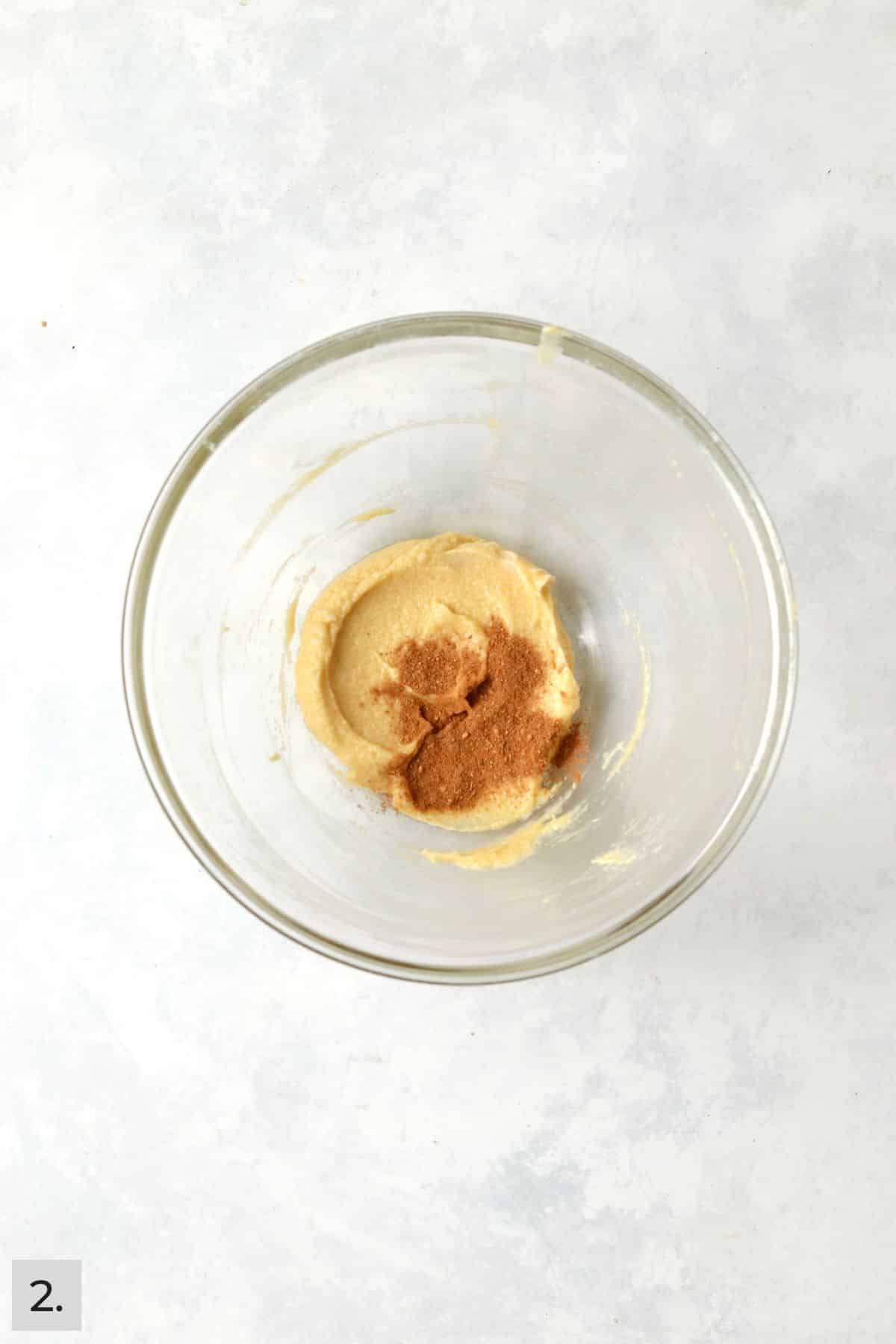 Chai spices being added to creamed butter and sugar in a glass bowl.