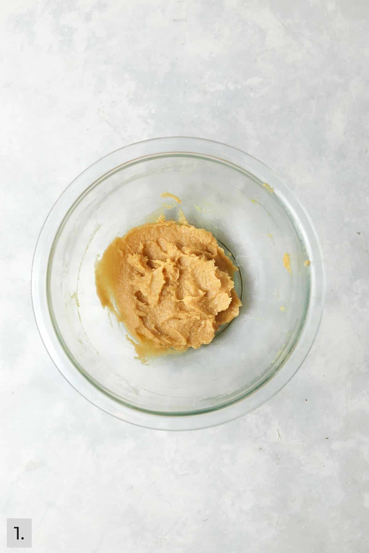 Butter and sugar creamed together with the egg yolk and vanilla in glass bowl.