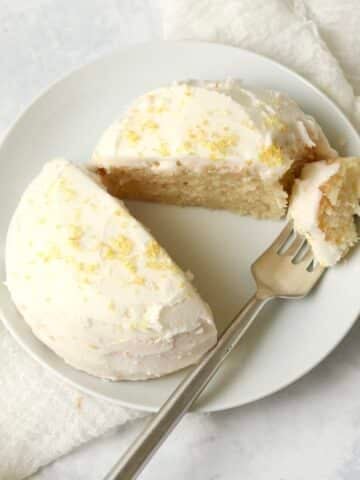Single serve lemon cake with frosting on a plate with a fork.
