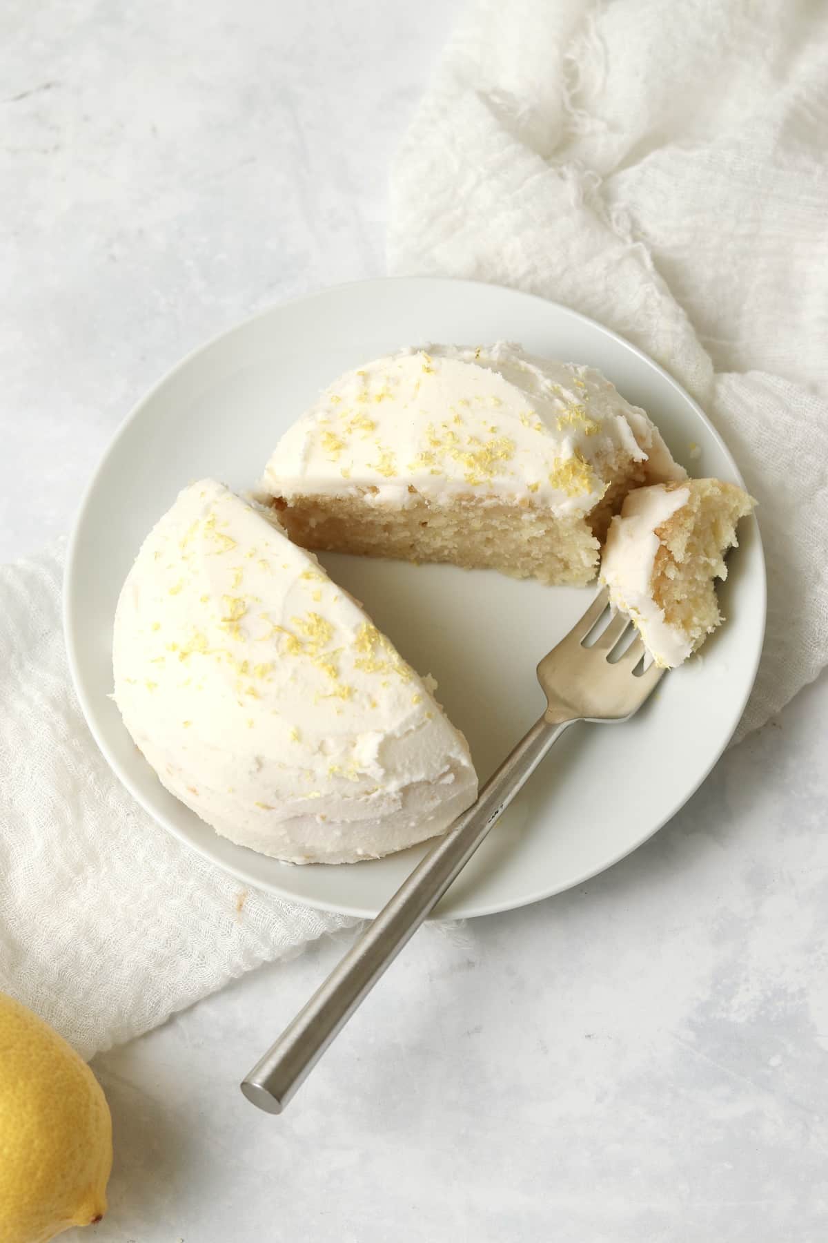 Single serve lemon cake with frosting on a plate with a fork.