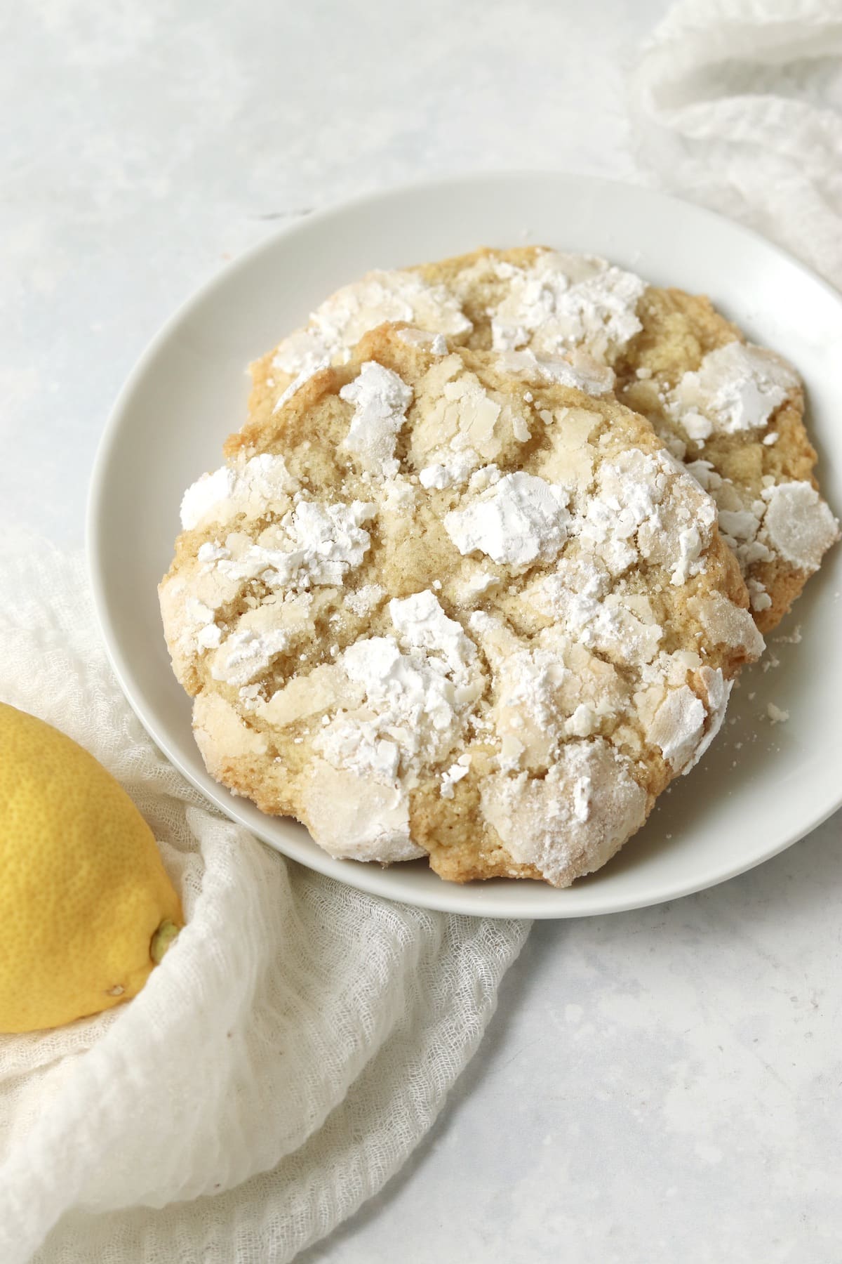 Single serve lemon crinkle cookie on a plate with a fresh lemon.
