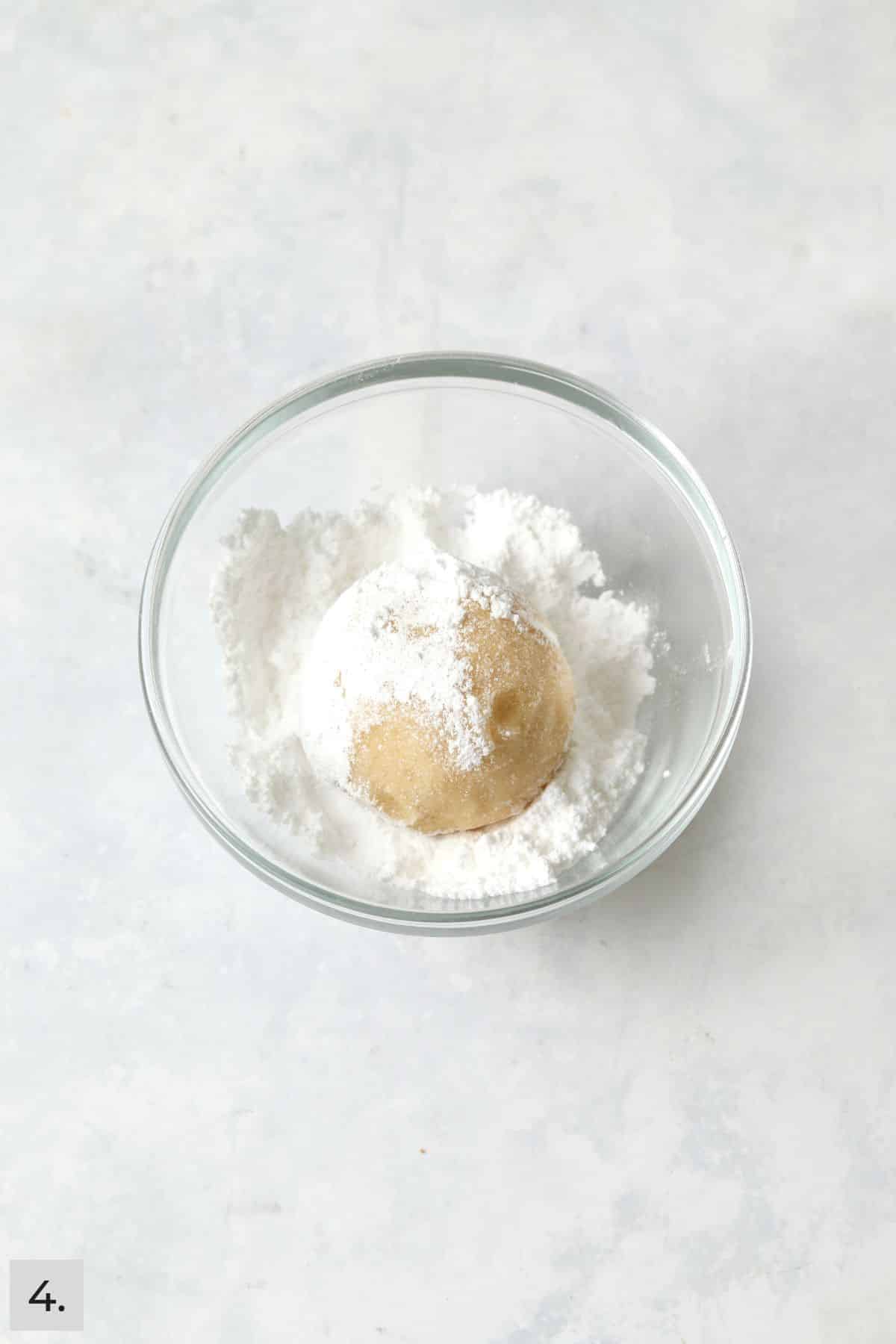Lemon cookie dough ball being rolled in powdered sugar.
