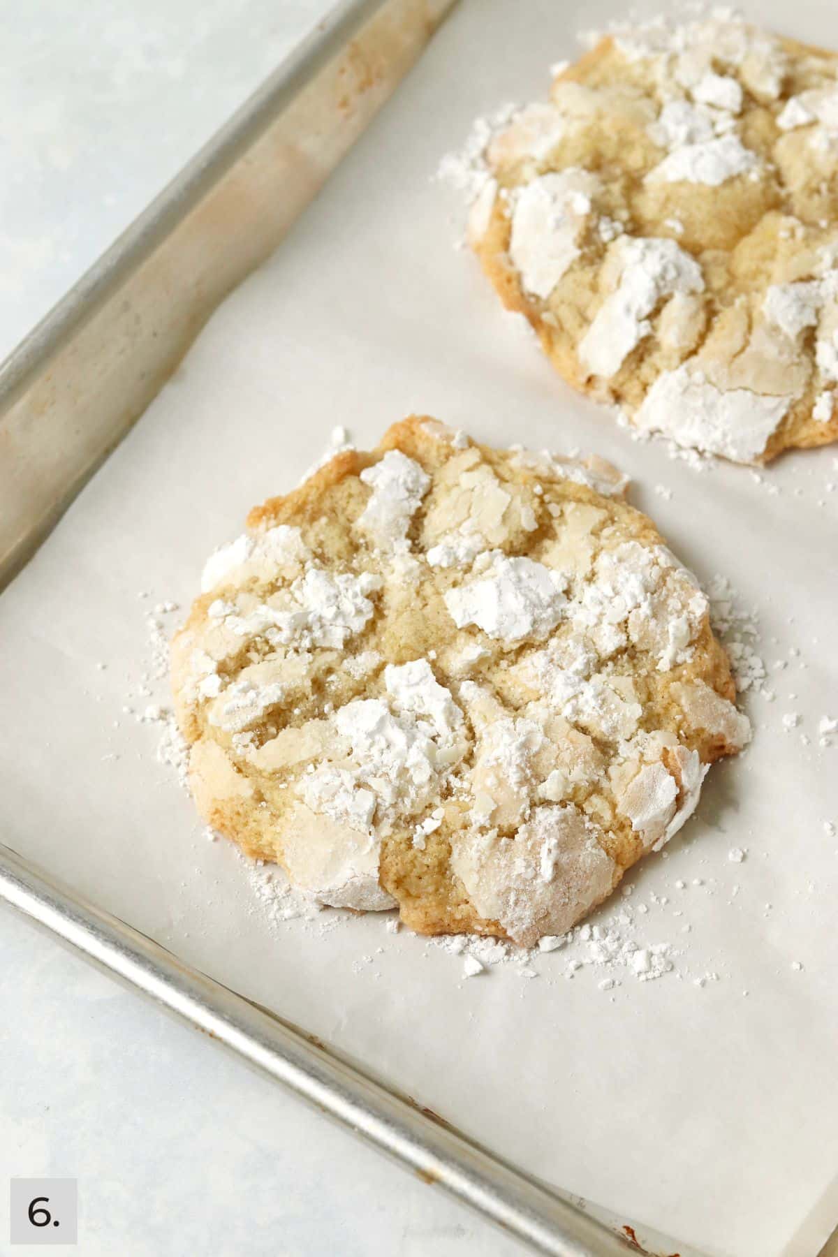 Two baked lemon crinkle cookies on a baking sheet.