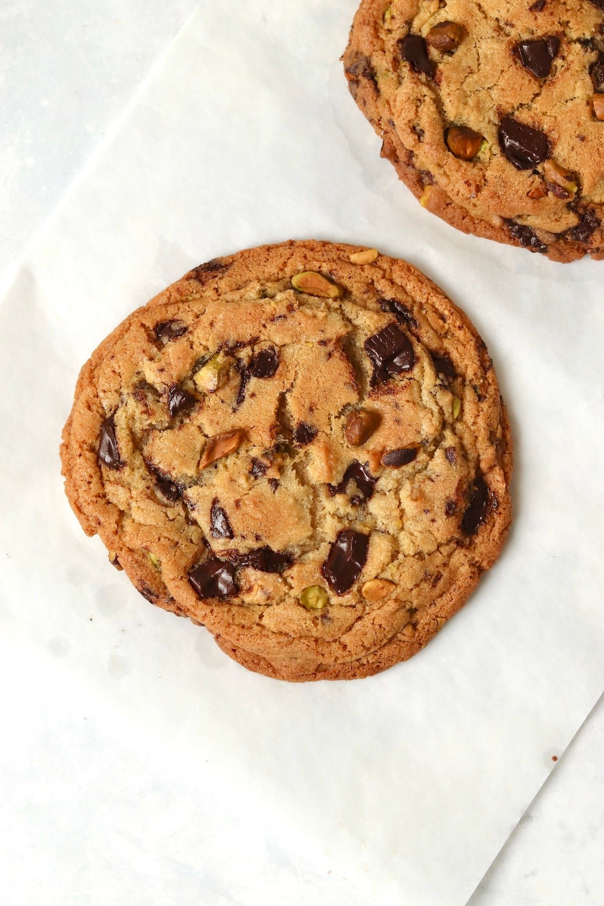 Baked single serve pistachio chocolate chunk cookie on parchment paper.