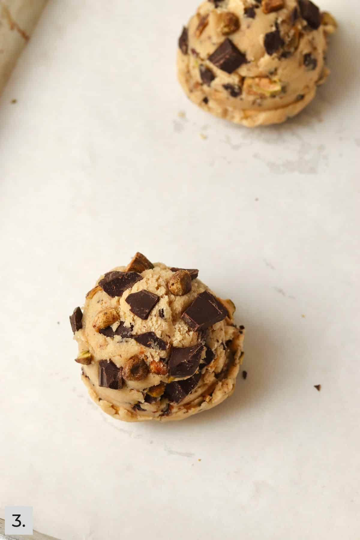 Two unbaked pistachio chocolate chunk cookies on a baking sheet.