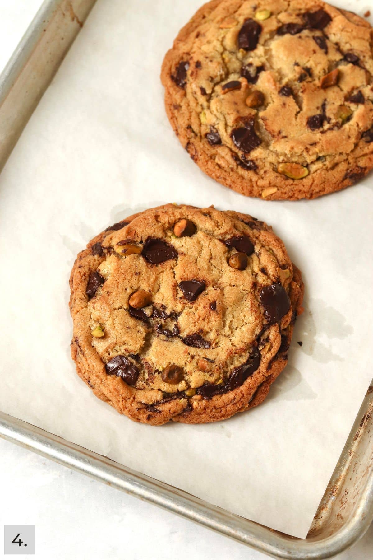 Two baked pistachio chocolate chunk cookies on a baking sheet.